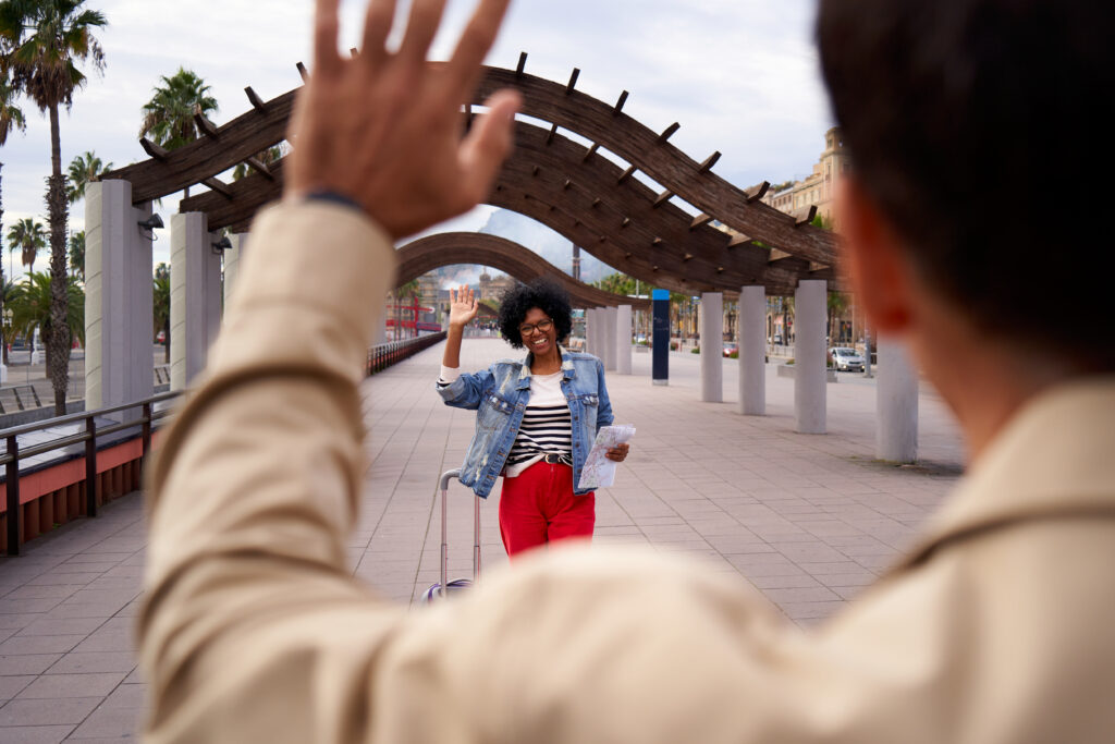 African American woman happily greeting her boyfriend with luggage outdoors after a long separation. Meeting in the street of two people who have not seen each other for a long time.